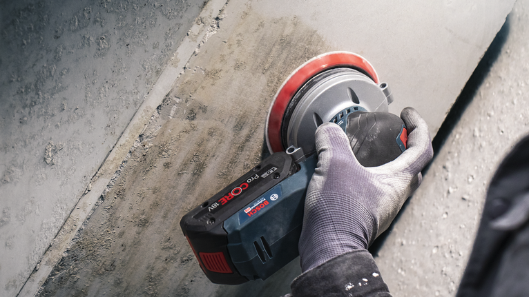 PRO F355 Sanding Disc, 150 mm, G400, 5 pcs Person wearing safety equipment grinds a concrete wall with a cordless tool.