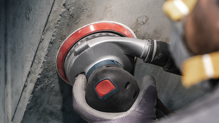 PRO F355 Sanding Disc, 150 mm, G400, 5 pcs Person wearing safety equipment uses a power sander on a concrete wall.
