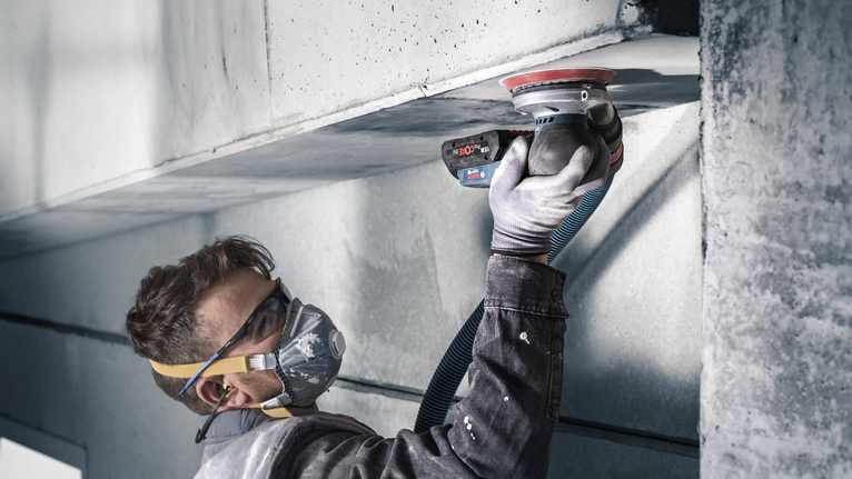 PRO F355 Sanding Disc, 150 mm, G400, 5 pcs Person wearing safety equipment uses a power sander on a concrete ceiling.