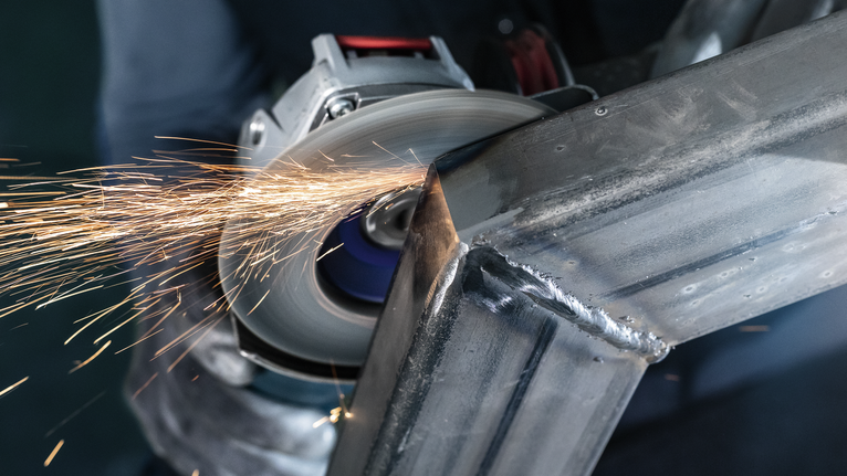 PRO X571 Flap Disc, Straight, 125 mm, G40, X-Lock Person wearing safety equipment grinds metal, creating sparks.