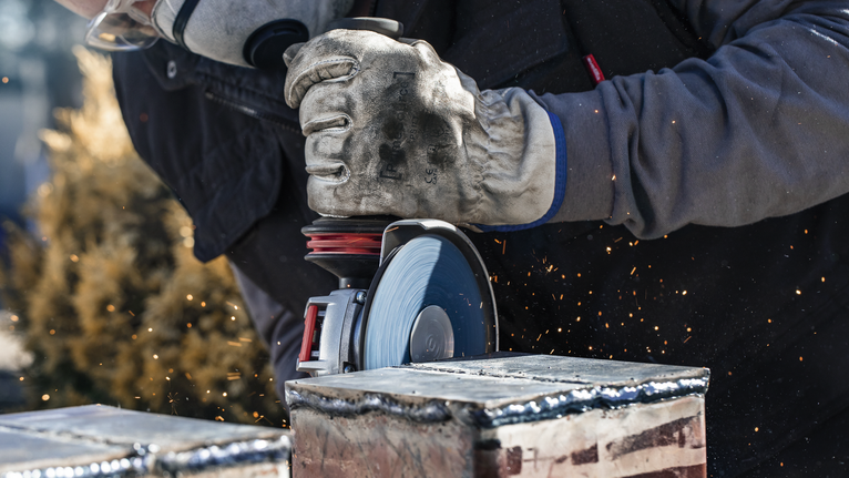 Person wearing safety equipment grinds metal, creating sparks.