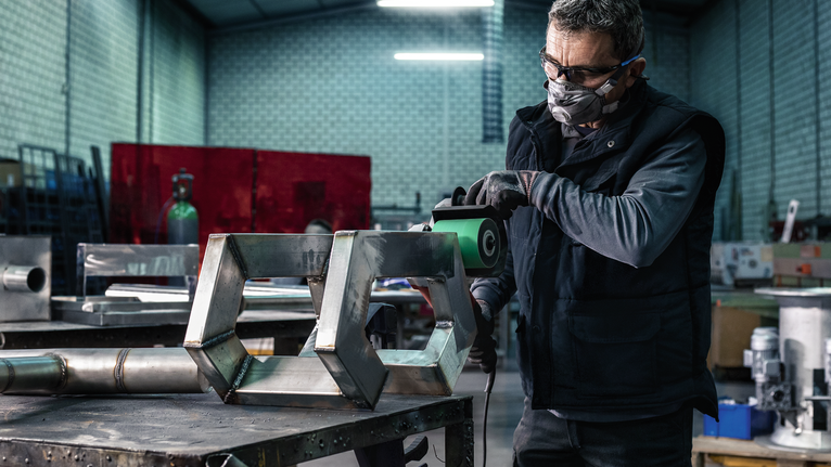 PRO Y580 Sanding Belt, 100 x 285 mm, 90 mm, G40, 5 pcs Person wearing safety equipment grinds a metal structure in a workshop.