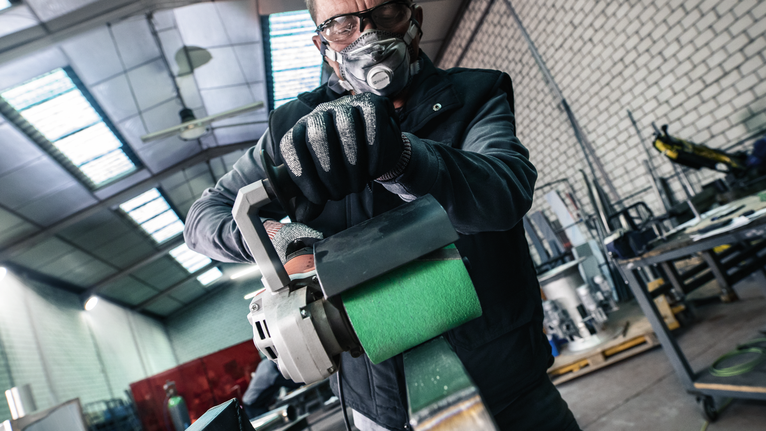PRO Y580 Sanding Belt, 100 x 285 mm, 90 mm, G40, 5 pcs Person wearing safety equipment operates an industrial grinder in a workshop.