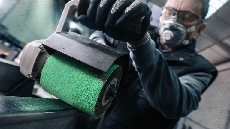 PRO Y580 Sanding Belt, 100 x 285 mm, 90 mm, G40, 5 pcs Person wearing safety equipment polishes a metal surface with a power sander.