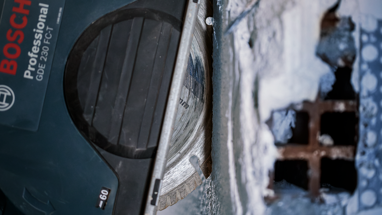 Diamond saw blade cutting through concrete near a metal grate.