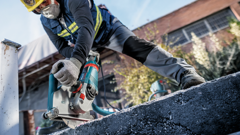 Person wearing safety equipment cuts concrete with a power cutter outdoors.