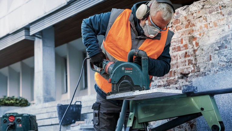 PRO Stone Diamond Disc, 180 x 22.23 mm A person wearing safety equipment cuts stone with a circular saw on a workbench.