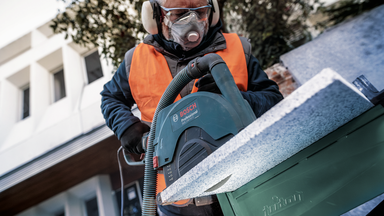 PRO Stone Diamond Disc, 180 x 22.23 mm Person wearing safety equipment cuts a stone slab with a large circular saw.