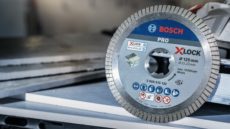 PRO Ceramic X-Lock Diamond Disc, 125 x 22.23 mm, 22.23 mm Diamond saw blade positioned on a worktable near stacked tiles.