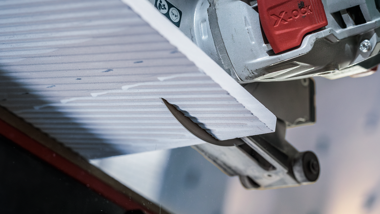 PRO Ceramic X-Lock Diamond Disc, 125 x 22.23 mm, 22.23 mm Circular saw cutting a textured tile panel in a close-up view.