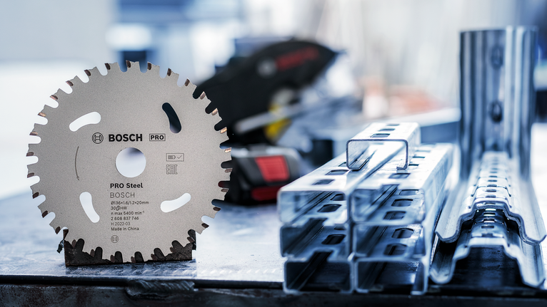 PRO Steel cordless Circular Saw Blade, 136 x 1.6 x 20 mm Circular saw blade standing upright on a workbench beside stacked metal beams.