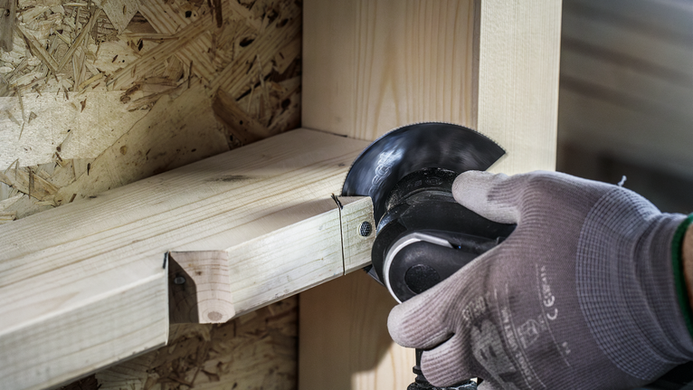 Person wearing safety equipment cuts wooden beams with an angle grinder.