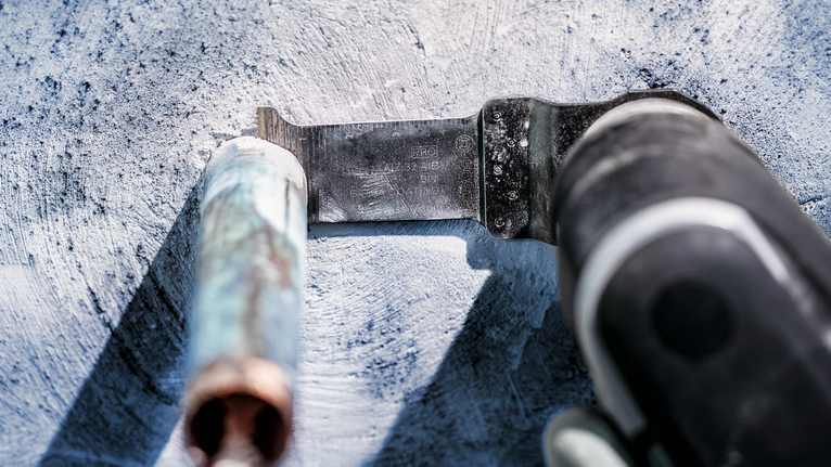 PRO AIZ 32 AIB Plunge Cut Blade, 32 x 50 mm, 5 pcs Oscillating tool cuts through a metal pipe on a concrete surface.