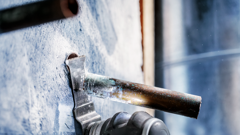 PRO AIZ 32 AIB Plunge Cut Blade, 32 x 50 mm, 5 pcs Power tool cuts through a metal pipe protruding from a concrete wall.