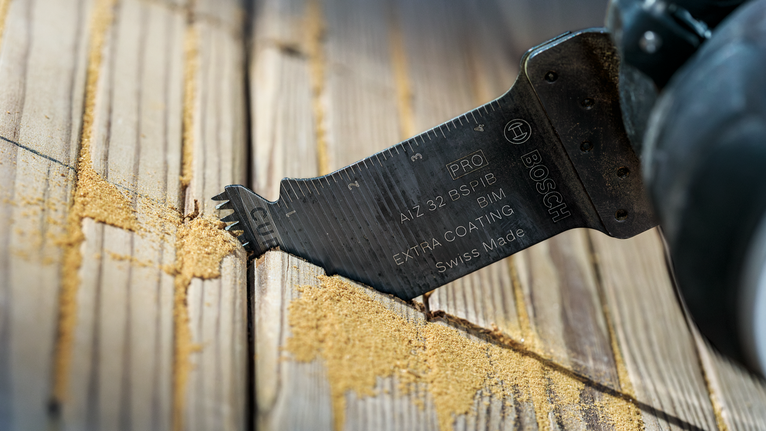 Oscillating multi-tool blade cutting through wooden planks and creating sawdust.