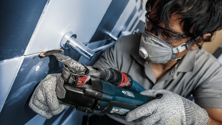 PRO MATI 68 RT3 Multitool Blade, 2.8 x 68 mm A person wearing safety equipment uses a power tool to cut tile around a pipe.