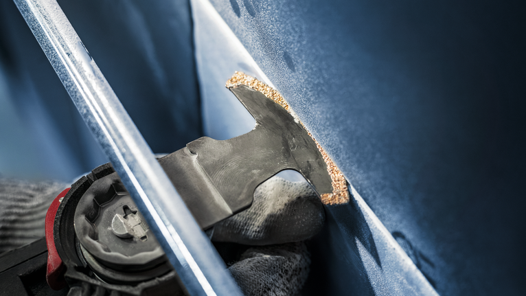 Person wearing safety equipment uses oscillating tool to cut a panel.