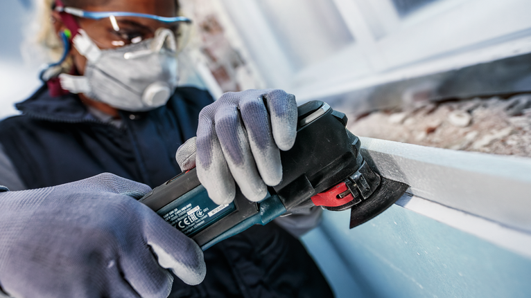 PRO ACZ 100 SWB Multitool Blade, 100 mm A person wearing safety equipment grinds a window frame with a power tool.