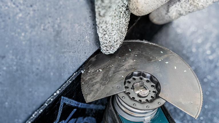 PRO ACZ 100 SWB Multitool Blade, 100 mm A person wearing safety equipment cuts concrete with an angle grinder.