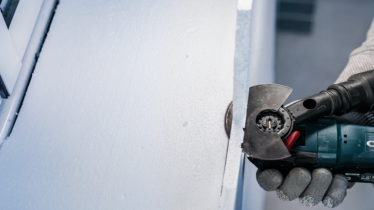 PRO ACZ 100 SWB Multitool Blade, 100 mm Person wearing safety equipment uses a power tool to cut a sheet of insulation.
