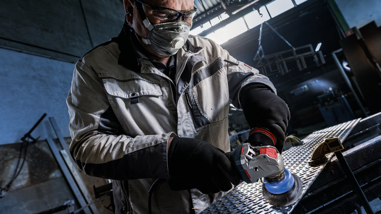 PRO Metal heavy X-Lock Cup Brush, 75 x 0.35 mm Person wearing safety equipment grinds a metal surface in an industrial setting.