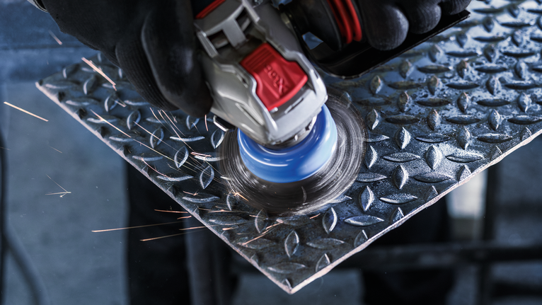 PRO Metal heavy X-Lock Cup Brush, 75 x 0.35 mm Person wearing safety equipment uses an angle grinder to polish a metal plate.