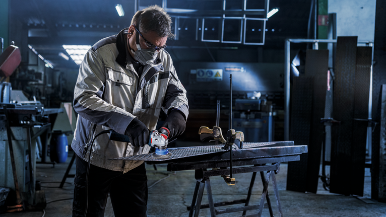 PRO Metal heavy X-Lock Cup Brush, 75 x 0.35 mm A person wearing safety equipment grinds a metal sheet in a workshop.