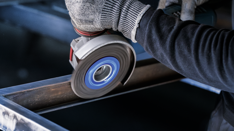 PRO Metal clean X-Lock Wire Wheel, 115 x 0.3 mm Person wearing safety equipment grinds a steel beam using an angle grinder.