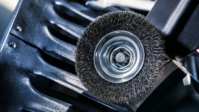 PRO Metal clean Bevel Brush, 100 x 0.3 mm, Thread Wire brush attachment on a power tool positioned above a metal surface.