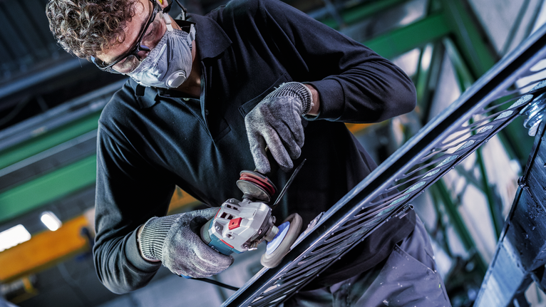 PRO Metal clean Bevel Brush, 100 x 0.3 mm, Thread Person wearing safety equipment uses an angle grinder to smooth metal.