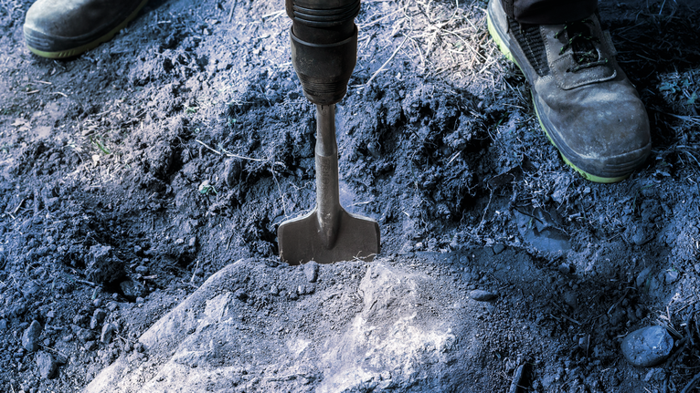 PRO SDS max Excavation Chisel, 110 x 400 mm Person wearing safety equipment uses a demolition tool to break hard soil.
