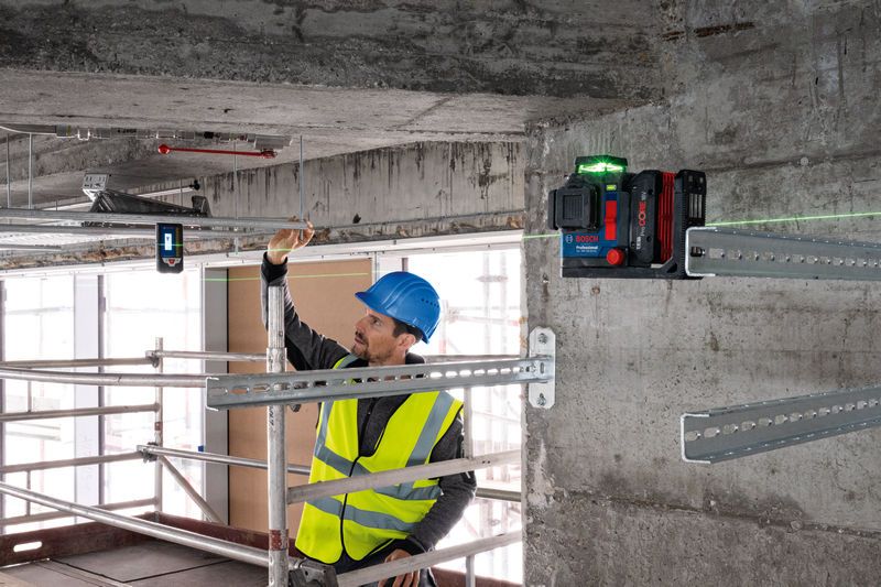 A person wearing safety equipment aligns metal framing using a laser leveling tool with a laser receiver.