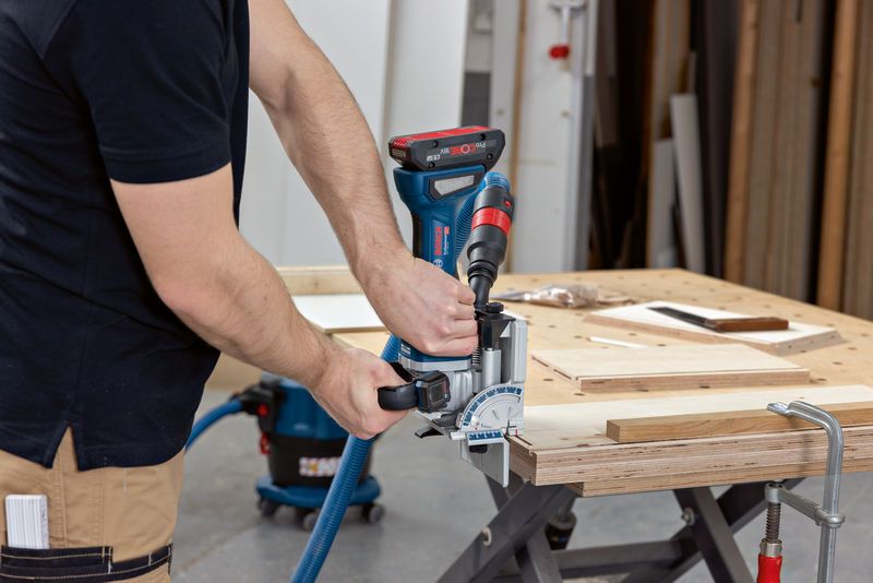 A person uses a biscuit joiner to cut slots into wooden boards on a workbench.