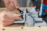 A person adjusts the fence on a biscuit joiner set on a wooden workbench.