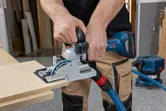 A person cuts a wooden board with a biscuit joiner connected to a dust extractor.