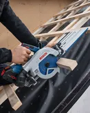 Person operating a circular saw to cut wood on a sloped roof frame.