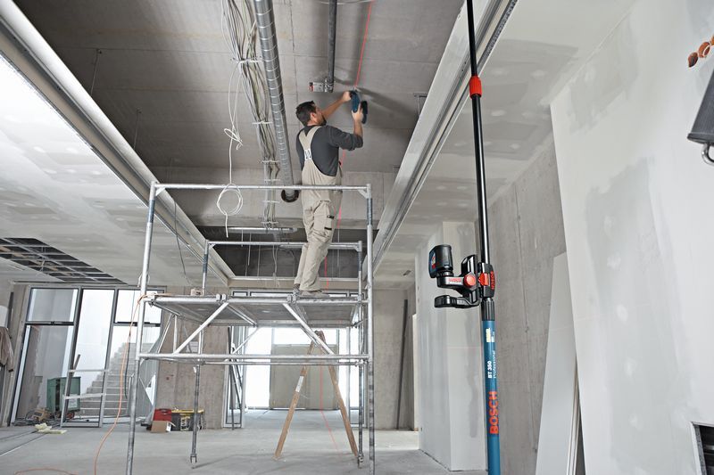 BM 1 A person wearing safety equipment works on a ceiling using a laser leveling tool on a universal mount.