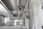 A person wearing safety equipment works on a ceiling using a laser leveling tool on a universal mount.