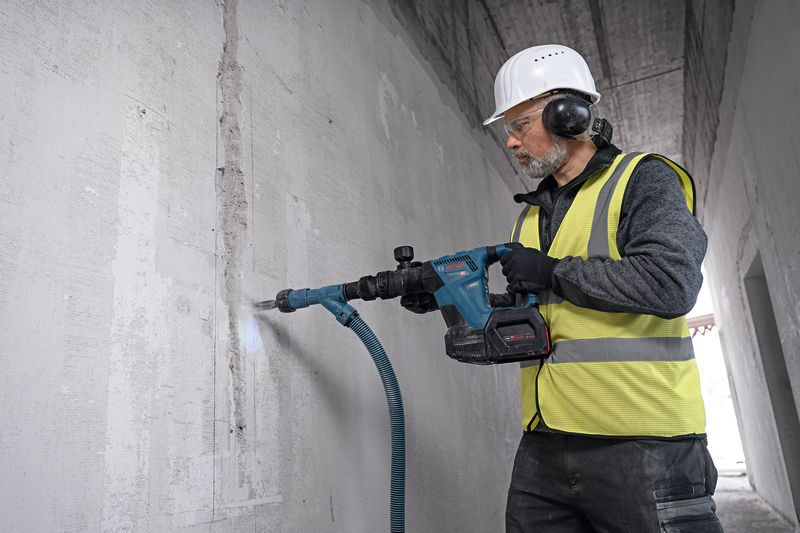 GSH 18V-5 A person wearing safety equipment uses a cordless demolition hammer to break a concrete wall.