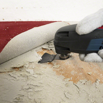HCS scraper ATZ 52 SC, rigid Person wearing safety equipment uses a multi-tool to remove adhesive under flooring.