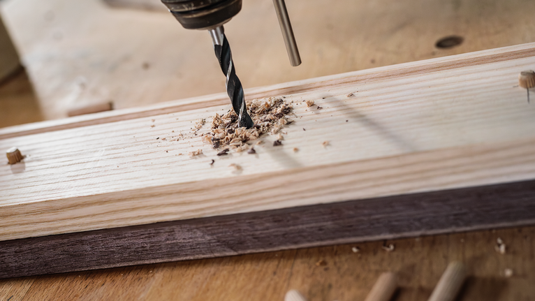 PRO Wood Brad Point Drill Bit Set, 8 pcs Drill creating a hole in a wooden board with wood shavings around the bit.