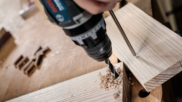 PRO Wood Brad Point Drill Bit Set, 8 pcs Person drilling a hole into a wooden plank on a workbench.
