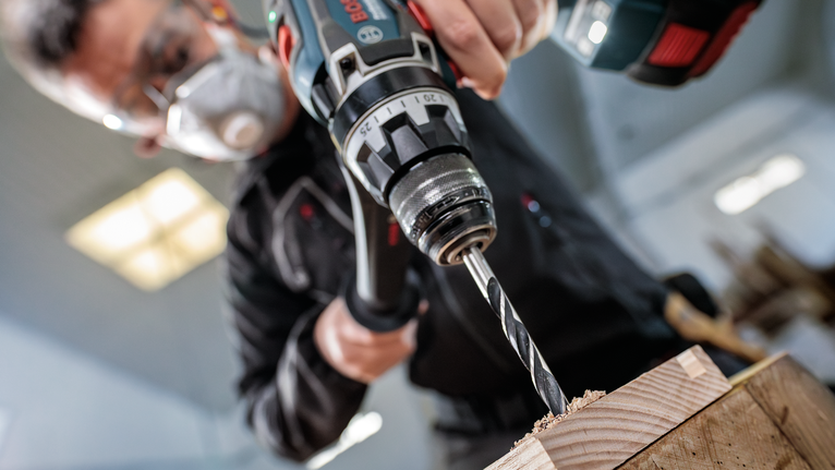 PRO Wood Brad Point Drill Bit Set, 8 pcs Person wearing safety equipment drills a hole into a wooden board.