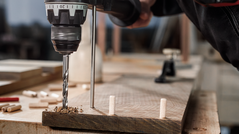 Person drilling holes into wooden boards for dowel joinery.