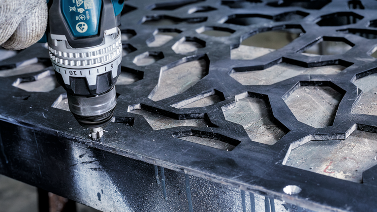 PRO Steel HSS Countersink Bit, 12 x 40 mm, M6 Person wearing safety equipment uses a drill to make a hole in a patterned metal sheet.