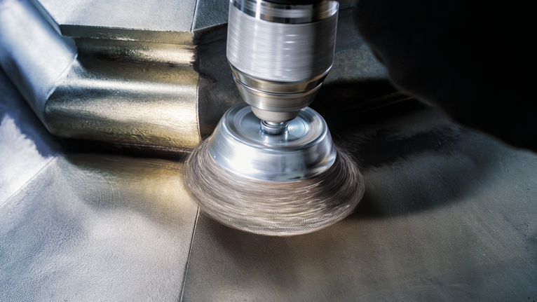 PRO Metal clean Cup Brush, Straight Shank, 50 x 0.2 mm A person wearing safety equipment polishes a metal surface with a rotary tool.