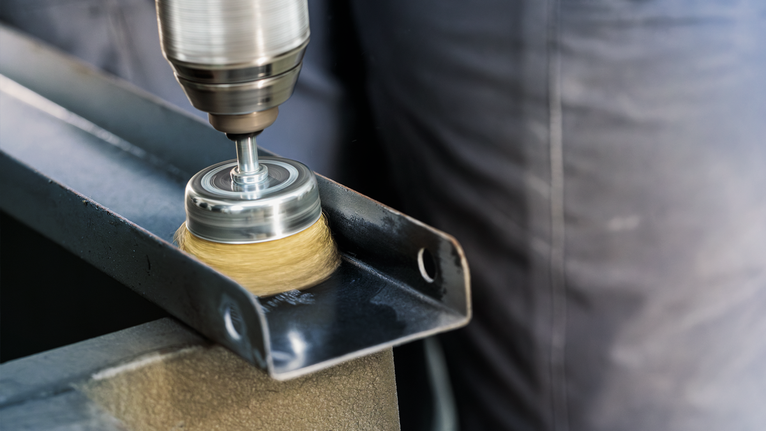 PRO Metal clean Cup Brush, Straight Shank, 50 x 0.2 mm A person uses a drill with a wire brush attachment to clean a metal beam.