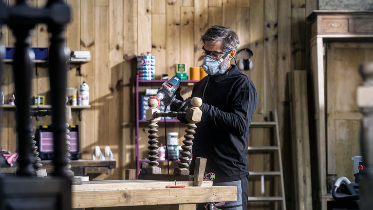 PRO Multi Material clean Cup Brush, 75 x 1 mm, Straight Shank Person wearing safety equipment sands a wooden chair leg in a workshop.