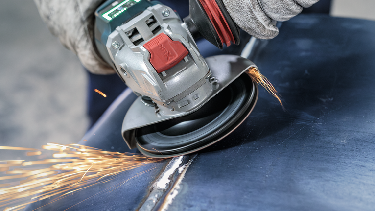 PRO Backing Pad Soft, 125 mm, X-Lock A person wearing safety equipment grinds a metal surface using an angle grinder.
