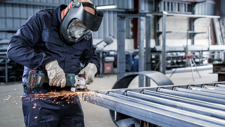 PRO Backing Pad Soft, 125 mm, X-Lock A person wearing safety equipment grinds metal, creating bright sparks in a workshop.